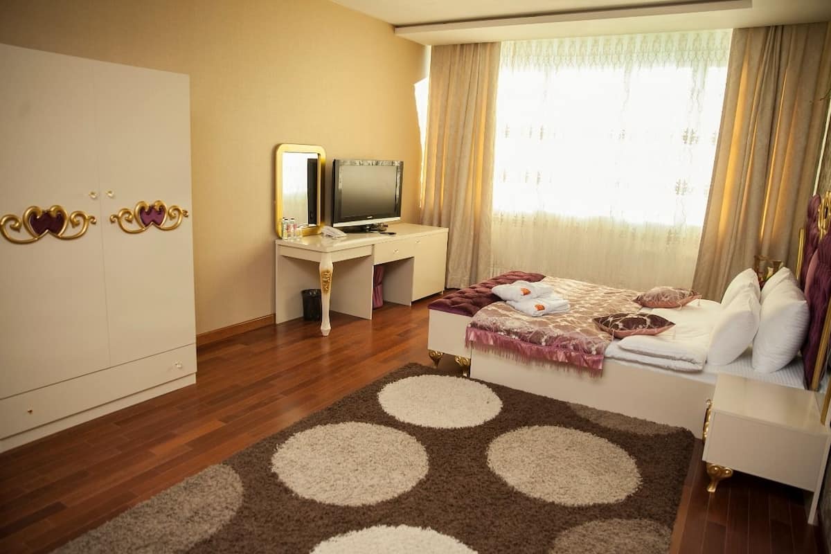 A hotel room with a bed, a desk with a TV, a wardrobe, and a large window with curtains.