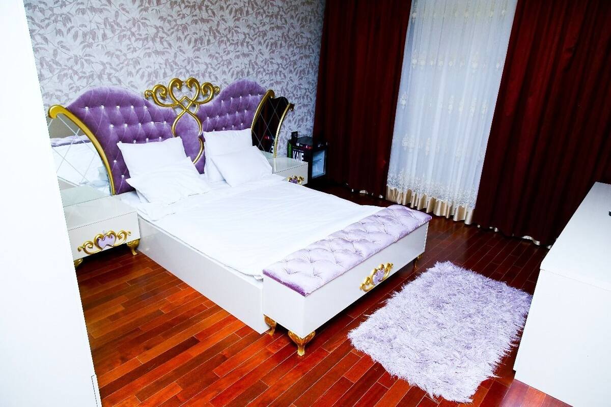 A bedroom with a large bed, a white nightstand, a dresser, and a fluffy rug.