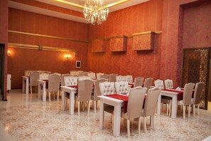 Un salón de conferencias con varias mesas y sillas, una araña de cristal y un panel decorativo en la pared.