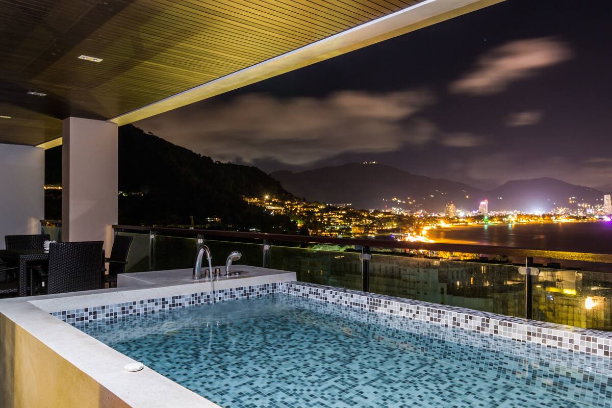 Une piscine sur le toit offrant une vue sur la ville, un espace salon et une rambarde en verre.