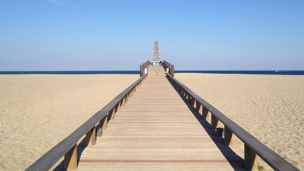 A wooden pier extending into a sandy beach with a clear blue sky above. - Rev'Hotel (Leucate)