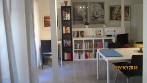 A modern living room with a white sofa, a coffee table, and a bookshelf filled with books. There are framed pictures on the wall and a small plant on the bookshelf.