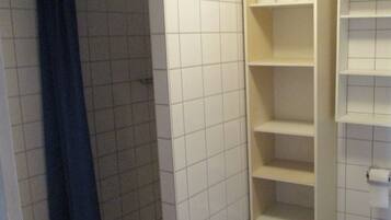 Ein Badezimmer mit Toilette, einer Dusche mit blauer Duschvorhang und einer weißen Ablage mit Toilettenpapier.