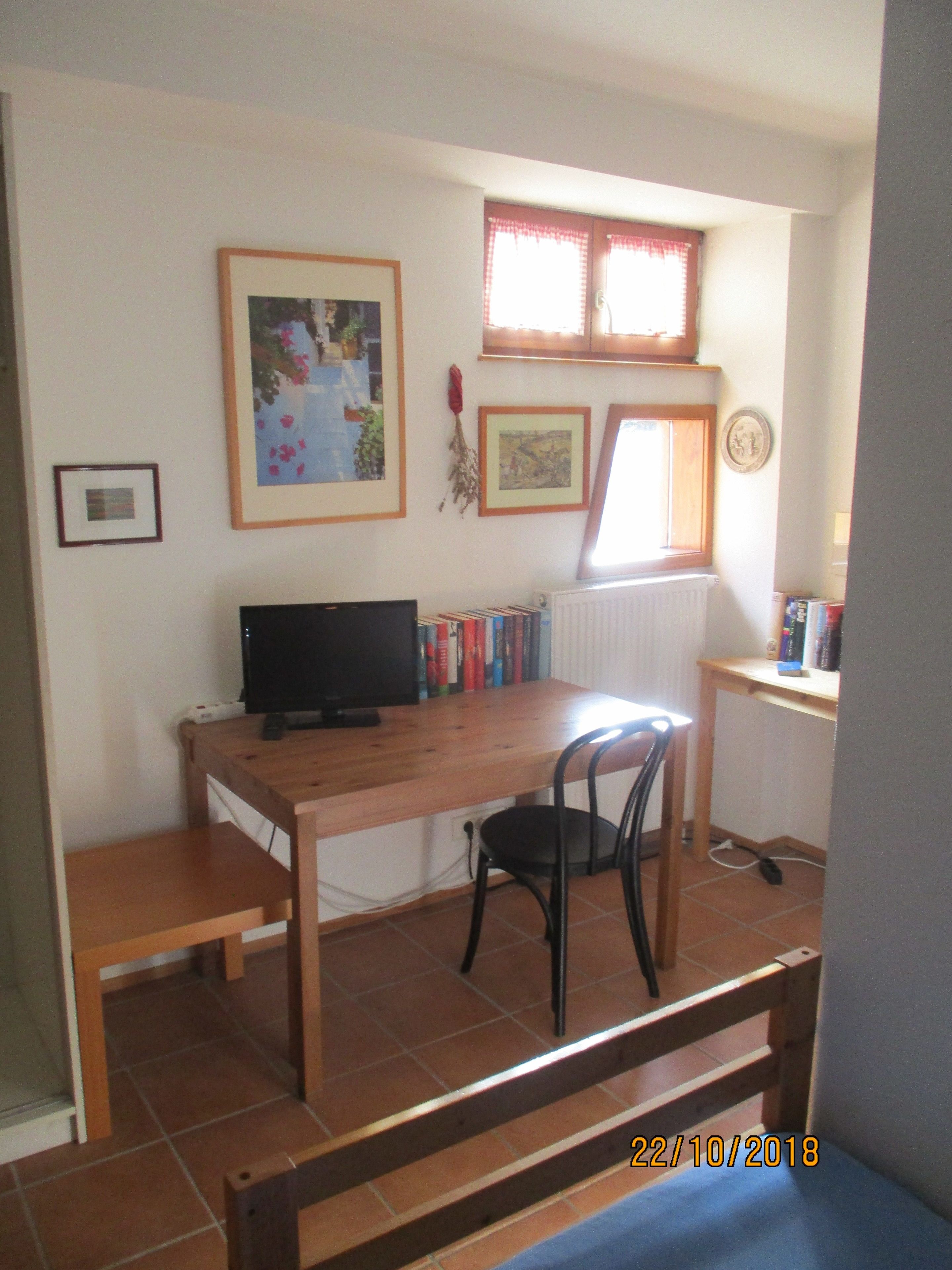 A small, tidy room with a wooden desk, a black chair, a television, and a bookshelf.