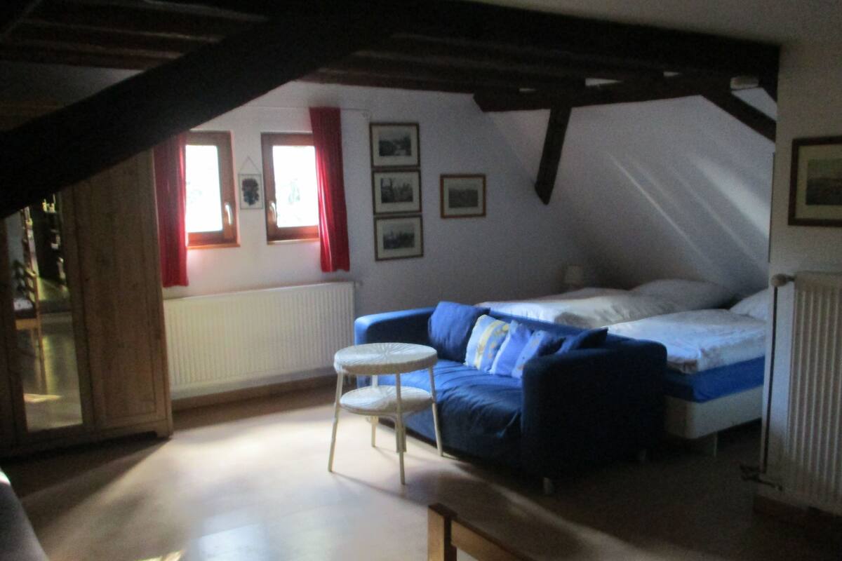 An attic bedroom with a bed, a small round table, and a sofa.