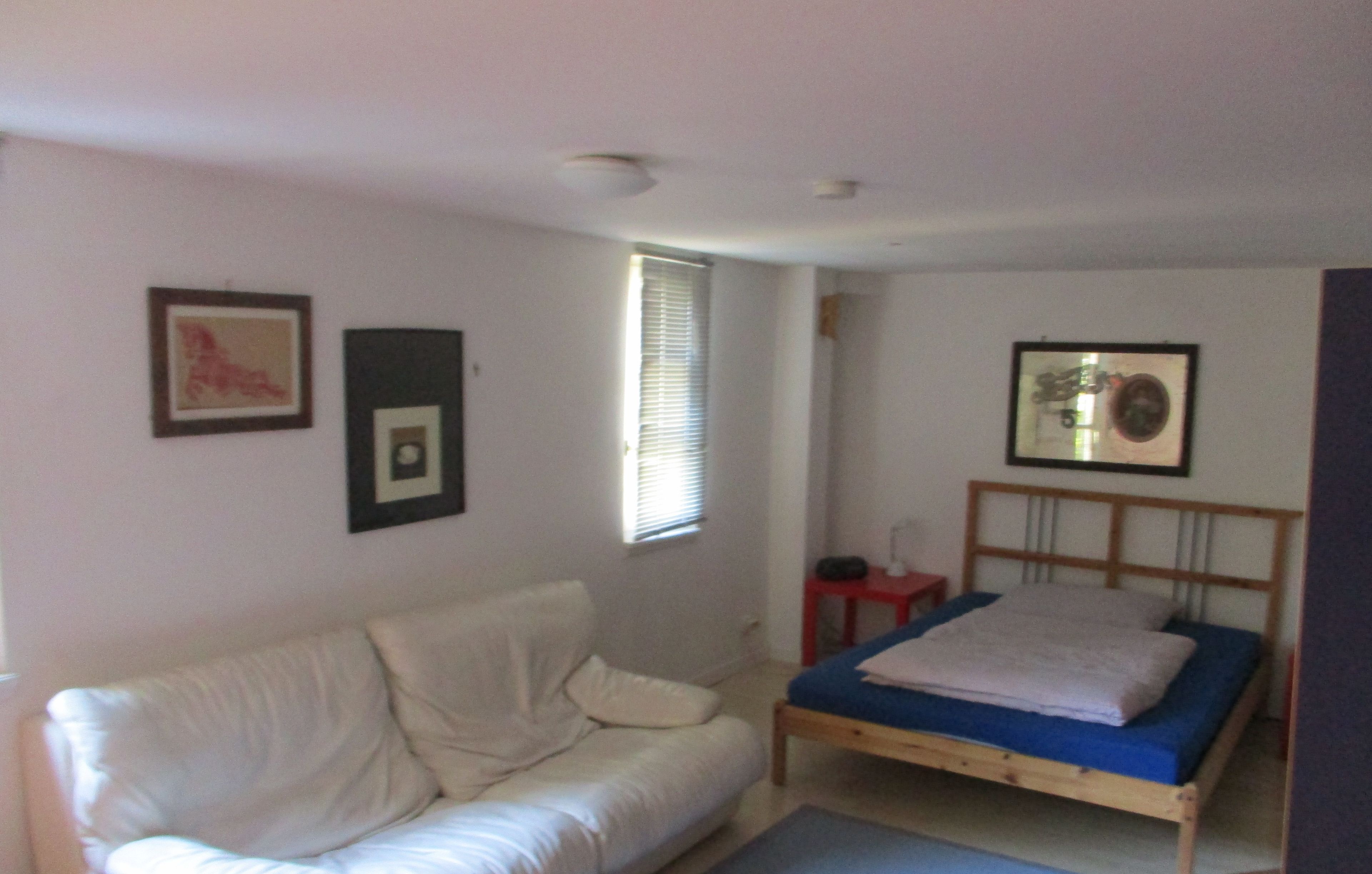 A bedroom with a bed, a wooden headboard, a white sofa, and a small bedside table.