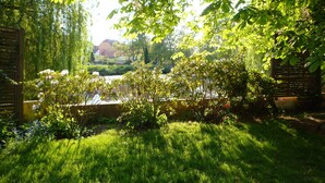 A lush garden with a variety of plants and flowers, a wooden fence, and a glimpse of a building in the background.