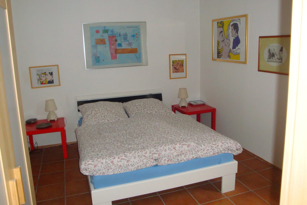 A bedroom with a bed, two bedside tables, and three framed pictures on the walls.