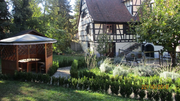 A traditional half-timbered house with a garden, a wooden gazebo, and a staircase leading to the entrance.