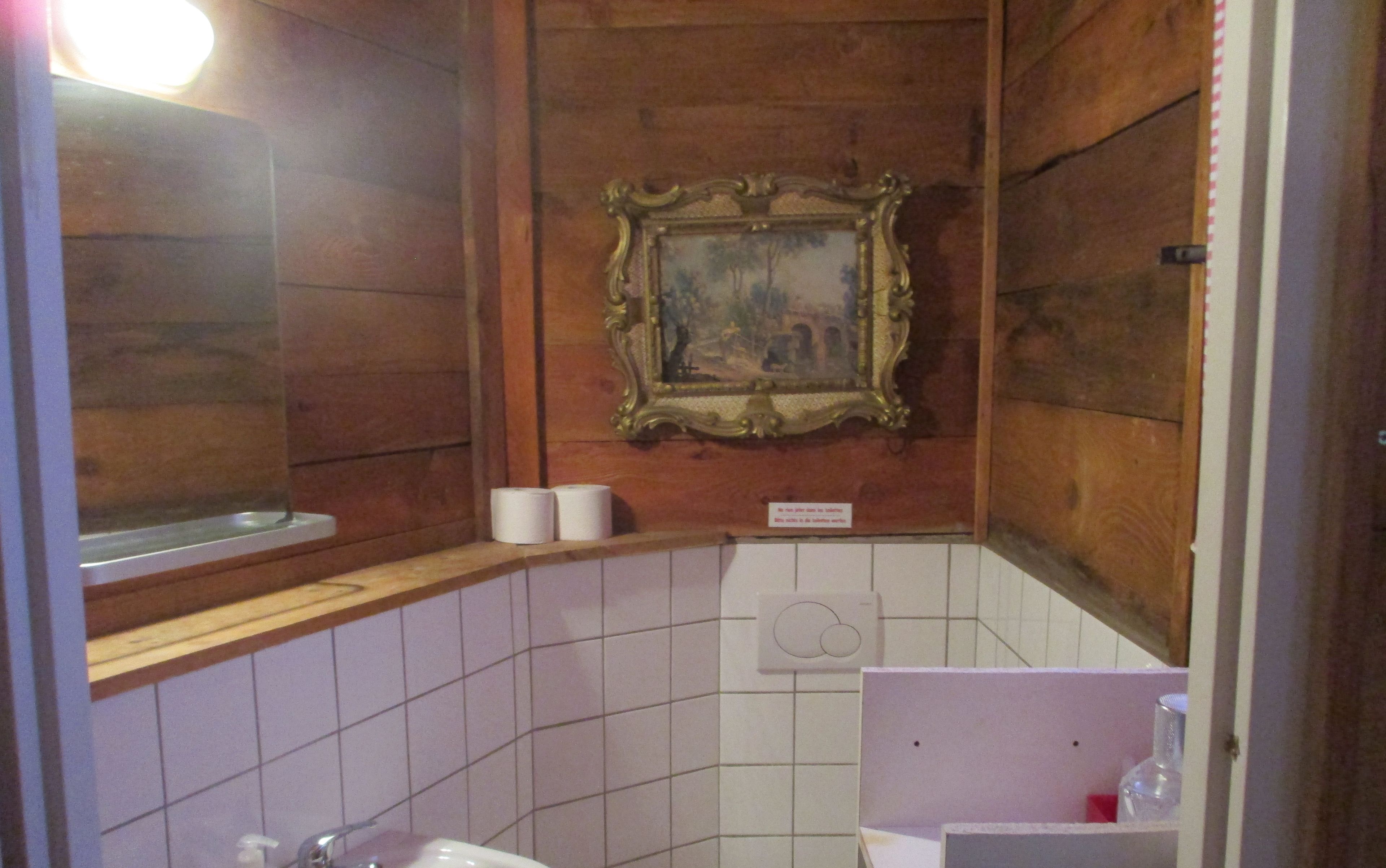 A bathroom with wooden walls, a tiled floor, a sink, and a framed painting on the wall.