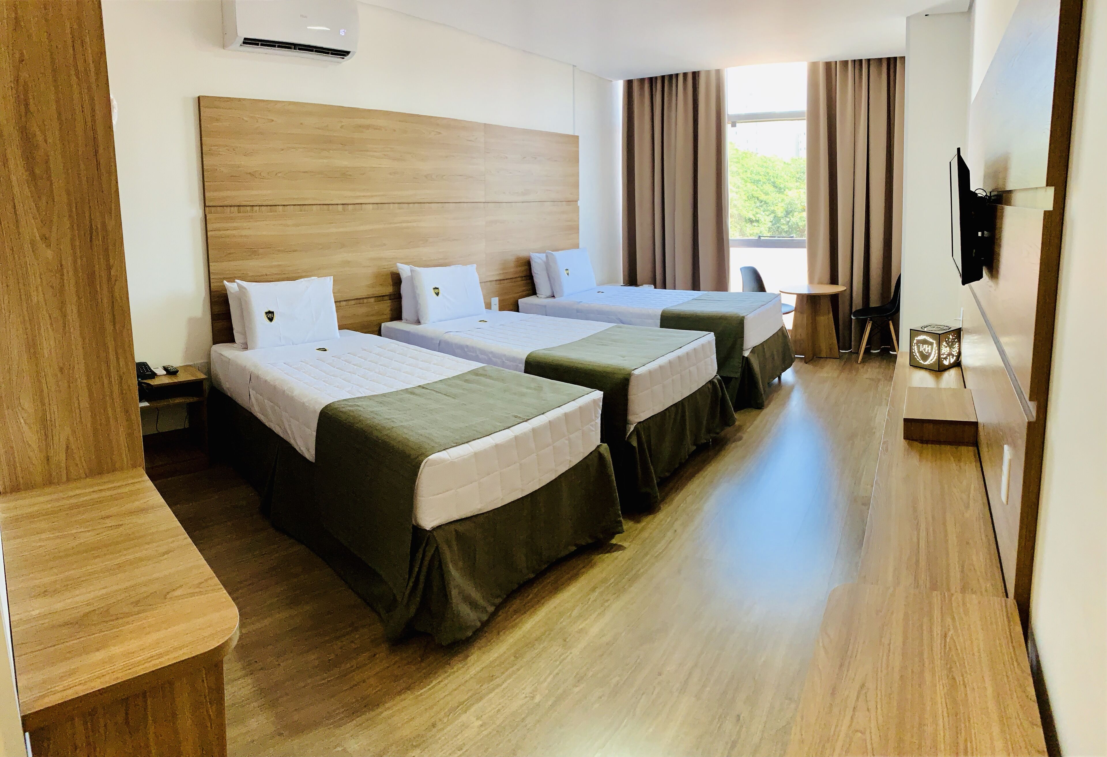 A hotel room with three beds, a wooden headboard, a TV, and a window with curtains.