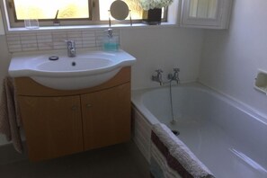 Un baño con lavamanos blanco, tocador de madera, bañera y ventana con vistas.