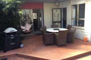 Un patio con una mesa redonda y sillas de mimbre, una silla colgante y un casco blanco en el suelo.