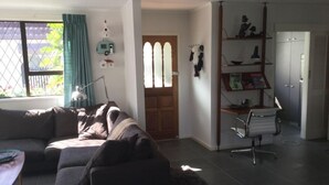 Un salon comprenant un canapé, un bureau et une chaise. On y trouve une porte avec une fenêtre et une étagère ornée d’objets décoratifs.