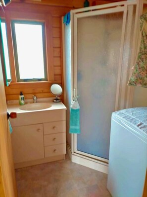 Un baño pequeño con ventana, espejo, lavabo y zona de ducha.