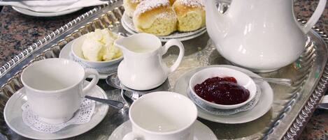 Un plateau avec des tasses à thé, une théière, un pot de crème, un bol de confiture et une assiette de scones.