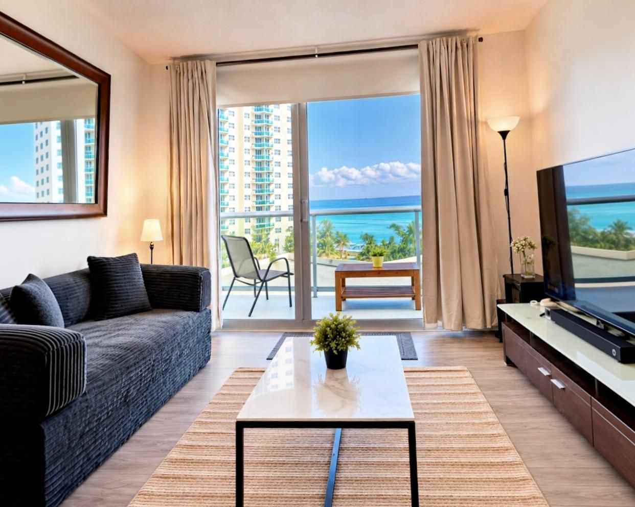 Een moderne hotelkamer met een bank, een salontafel, een televisie en een balkon met uitzicht op de oceaan.