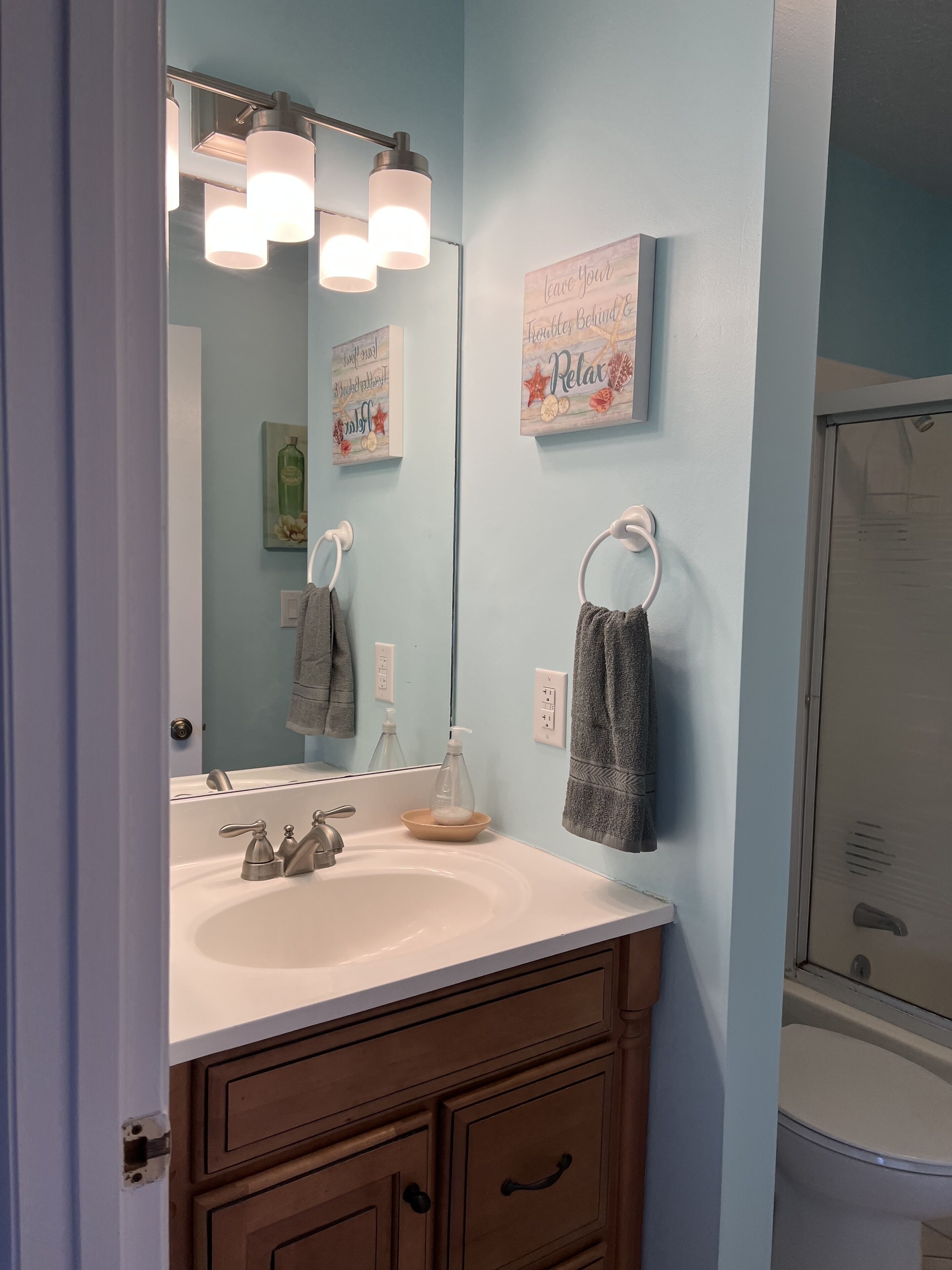 Une salle de bain avec un lavabo blanc, un miroir, un porte-serviettes et une douche.