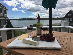 Une terrasse en bois sur laquelle se trouve une planche à découper en marbre, un morceau de fromage, un couteau, une bouteille de vin et un verre de vin rouge.