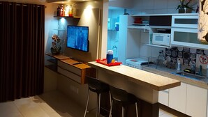 Uma cozinha moderna com uma ilha central, banquetas, televisão e ventoinha no teto.