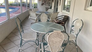 Un área de patio techada con una mesa redonda de vidrio y sillas de mimbre.