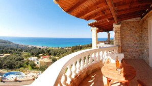 Un balcón con una pérgola de madera, paredes de piedra y vistas al mar y al paisaje.