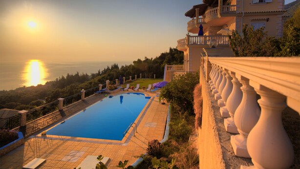 Una piscina con vistas al mar, una casa grande con balcones y un cielo despejado.