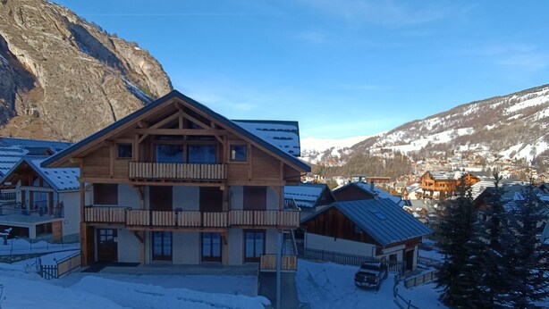 Una cabaña de madera de varios pisos con balcones, rodeada de montañas nevadas y un cielo despejado.