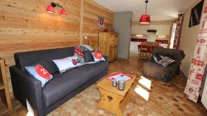 Un salón acogedor con un sofá oscuro, una mesa de centro de madera y una alfombra estampada.