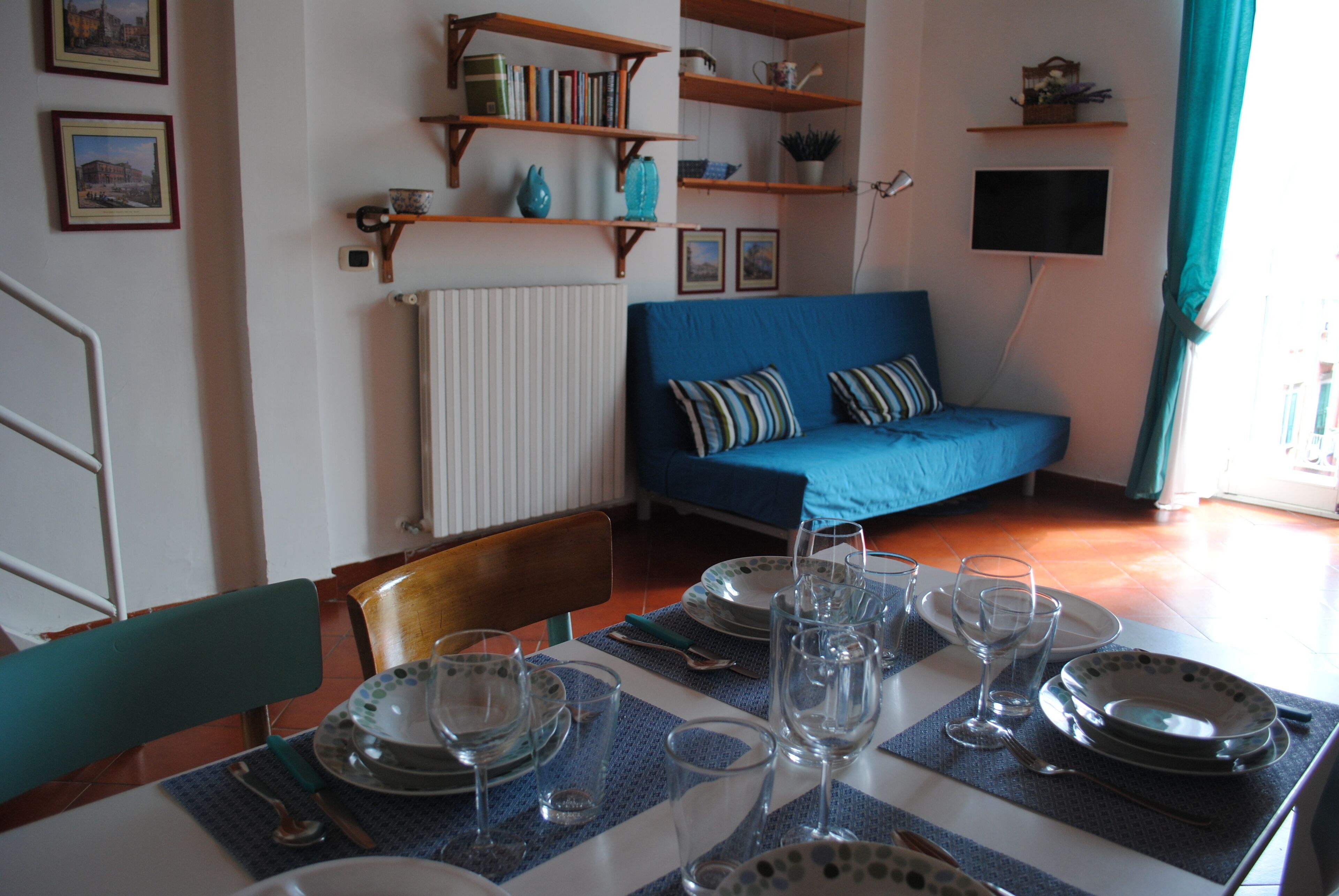 Un coin repas avec une table dressée pour quatre personnes, des chaises, un canapé bleu et des étagères remplies de livres et d’objets décoratifs.