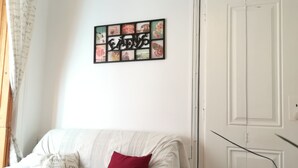 Une pièce avec un canapé blanc, un coussin rouge, une œuvre d’art murale et une porte blanche.