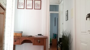 Un couloir avec un bureau en bois, trois tableaux encadrés accrochés au mur et une plante en pot.