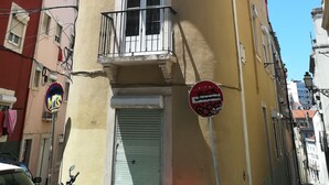 Un immeuble d’angle avec un balcon, un volet fermé et un panneau indiquant qu’il est interdit de se garer.