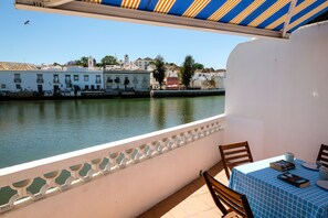 Ein Balkon mit Tisch und Stühlen mit Blick auf einen Fluss und Gebäude im Hintergrund.