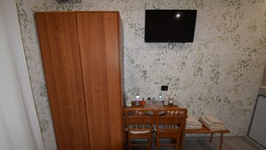 A room with a wooden wardrobe, a television mounted on the wall, a small table with chairs, and a tiled floor. - Room Vichy (Roma)