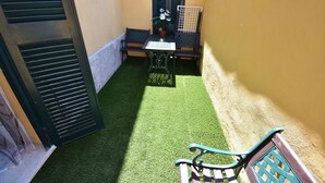 A small outdoor patio with artificial grass, a table, two chairs, and a potted plant. - Room Vichy (Roma)
