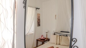A bedroom with a bed, a bedside table, a lamp, and a window with curtains. - Villa Andreas (Hydra)