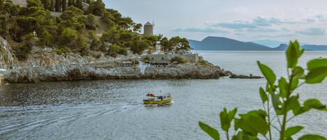 A coastal scene with a boat on the water, rocky terrain, and buildings on a hillside.