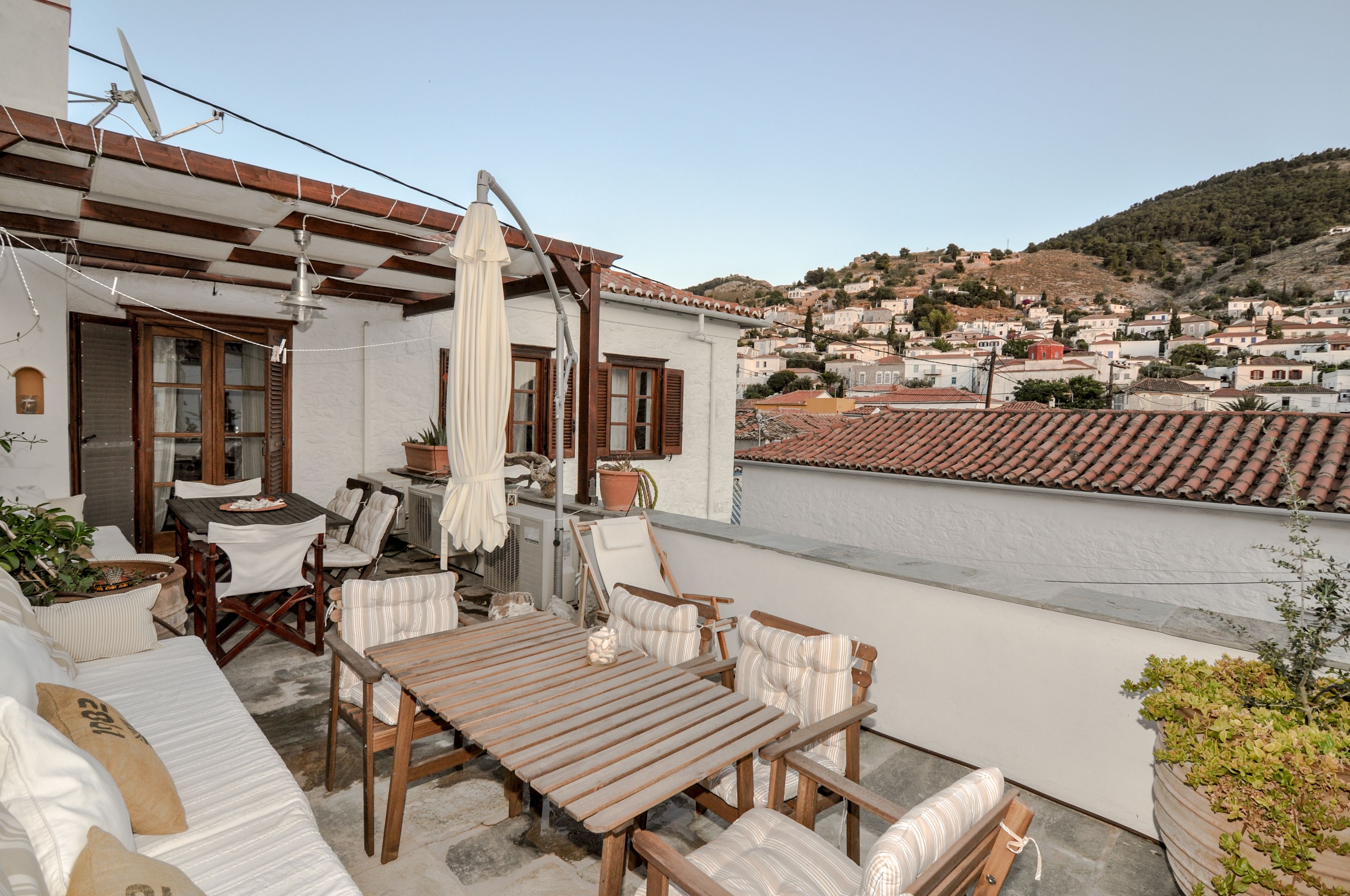 A rooftop terrace with a wooden table and chairs, a white umbrella, and potted plants.