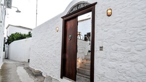 A narrow stone pathway leading to a white building with a wooden door and two wall-mounted lights. - Villa Andreas (Hydra)