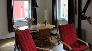 A dining area with a round table, four chairs, a vase with flowers, and two windows with curtains. - Family-friendly spacious and luxurious detached vacation home for 8 to 9 people (Lenterode)