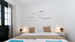 A double bed with two blue towels, a bedside table with a lamp and a plant, and a wall with multilingual "Good Night" signs.