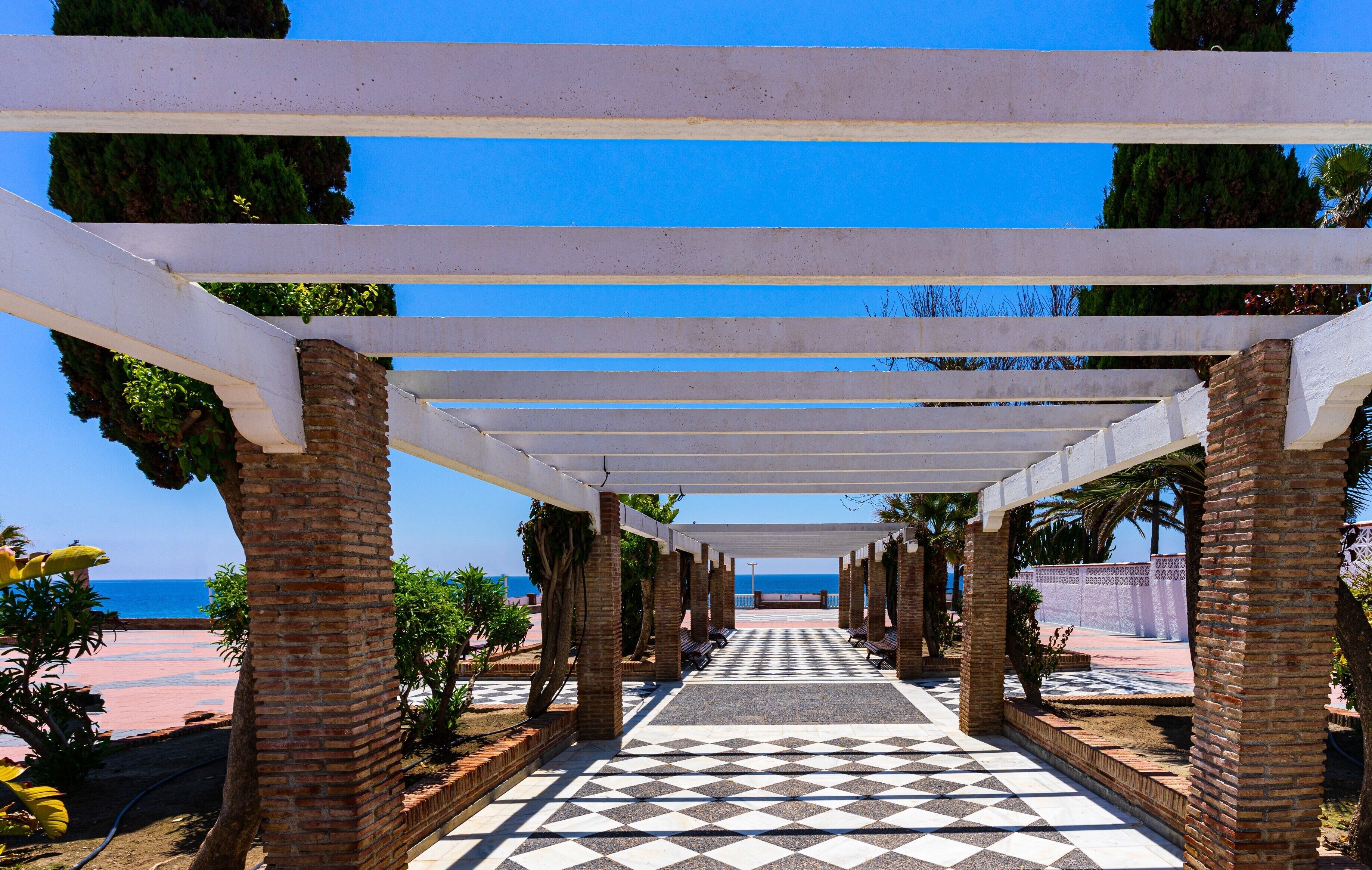 A covered walkway with a checkered floor leading to a beach.