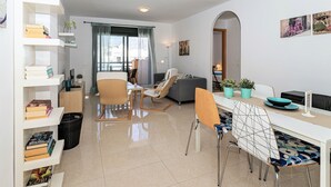 A modern living room with a dining area, a sofa, a coffee table, and a bookshelf.