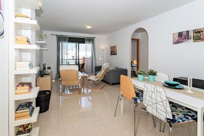 A modern living room with a dining area, a sofa, a coffee table, and a bookshelf.