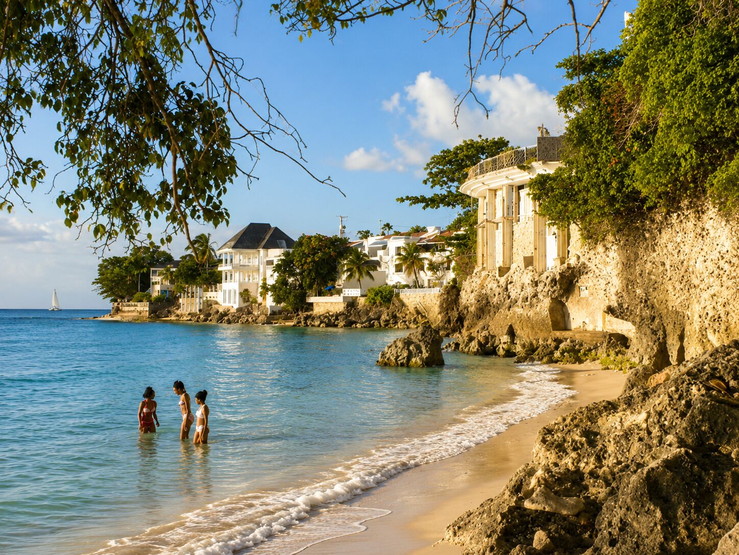 A coastal scene with a beach, rocky shoreline, and buildings with balconies overlooking the sea.