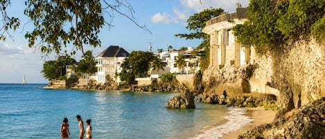 A coastal scene with a beach, rocky shoreline, and buildings with balconies overlooking the sea.