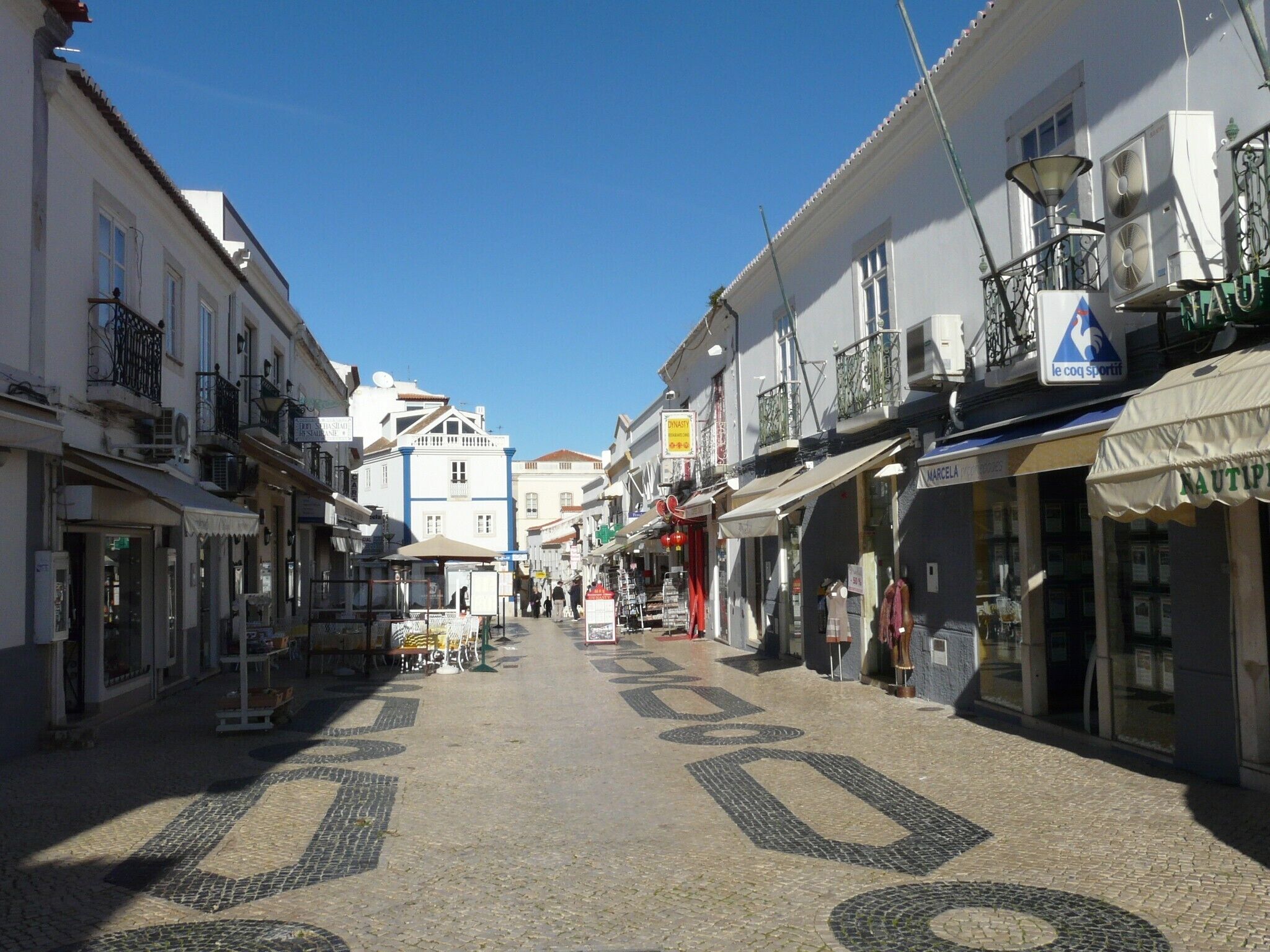 A cobblestone street lined with buildings, some with balconies and awnings.