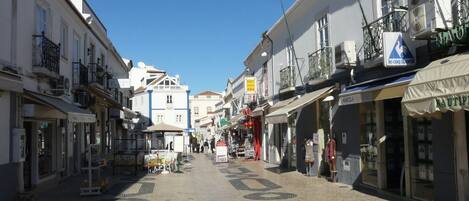 A cobblestone street lined with buildings, some with balconies and awnings.