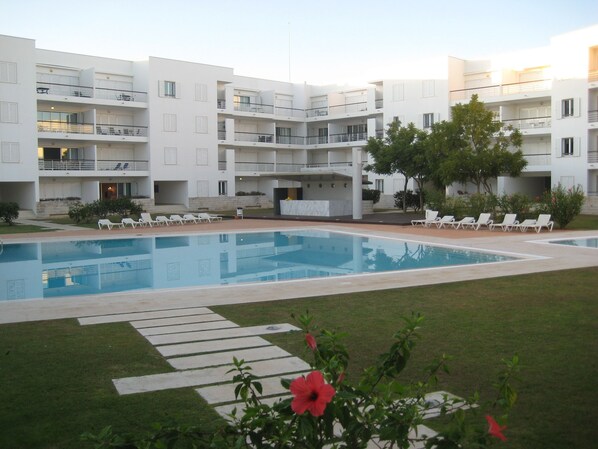 A modern apartment building with a central swimming pool, multiple balconies, and outdoor seating areas. - Homey Luxury Apartment | Direct access to pool | Close to beach & town (Lagos)